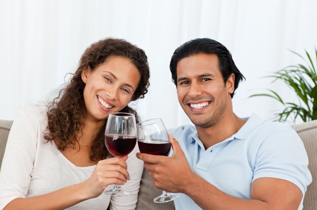 Heureux couple buvant du vin rouge assis sur le canapé