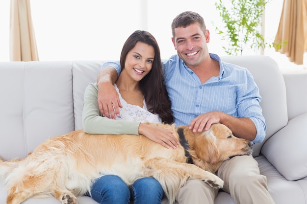 Heureux couple caresser le chien tout en étant assis sur le canapé