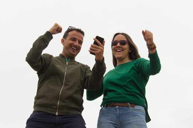 Heureux couple célébrant la victoire en regardant le téléphone portable sur fond blanc Jeune femme enthousiaste