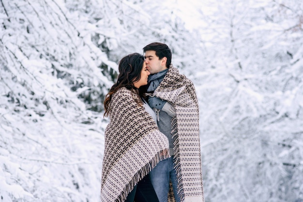 Heureux couple charmant recouvert d'une couverture chaude et marchant dans un parc enneigé