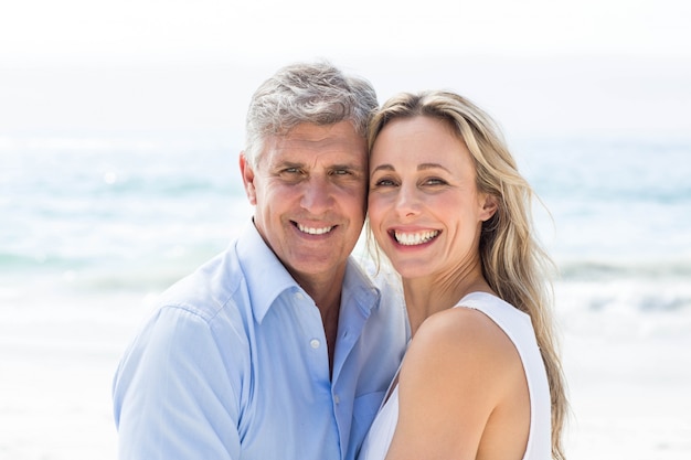 Heureux couple debout au bord de la mer et souriant à la caméra