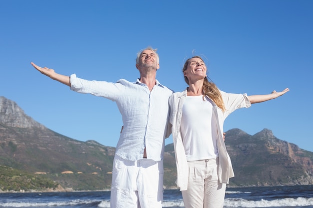 Heureux couple debout avec les bras tendus à la plage