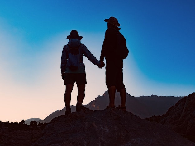 Heureux couple debout ensemble au sommet de la montagne et en regardant une vue imprenable au coucher du soleil