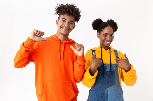 Heureux couple debout ensemble et pointant du doigt sur eux-mêmes, isolé sur mur blanc