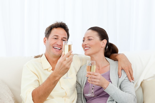 Heureux couple dégustation de champagne assis sur le canapé