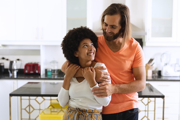 Heureux couple diversifié dans la cuisine souriant et embrassant. rester à la maison en isolement pendant le confinement en quarantaine.