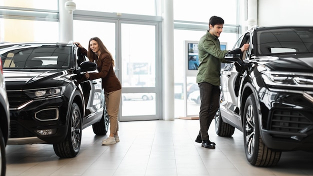 Heureux couple du millénaire sélectionnant une nouvelle voiture achetant ou louant une automobile à la bannière du concessionnaire automobile