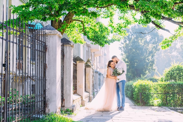 Heureux couple à l'extérieur par des arbres verts Beau mec barbu étreint une femme dans une robe