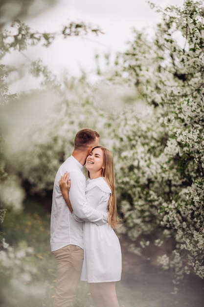 Heureux couple familial amoureux dans un verger de pommiers en fleurs au printemps. Une famille heureuse s'amuse en se promenant dans le jardin. L'homme tient la main de la femme. Relations de famille