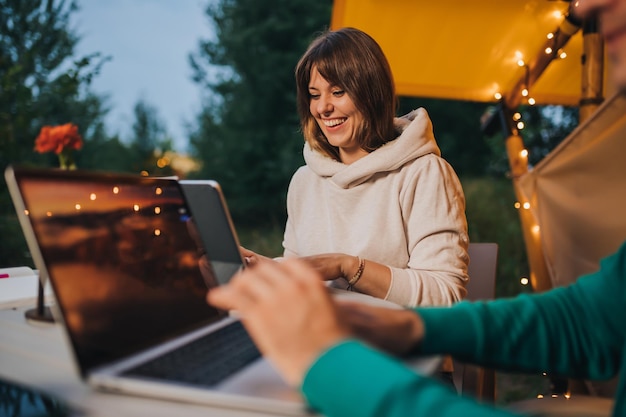 Heureux couple de famille indépendants travaillant sur un ordinateur portable sur une tente de glamping confortable en soirée d'été Tente de camping de luxe pour des vacances en plein air et des vacances Concept de style de vie