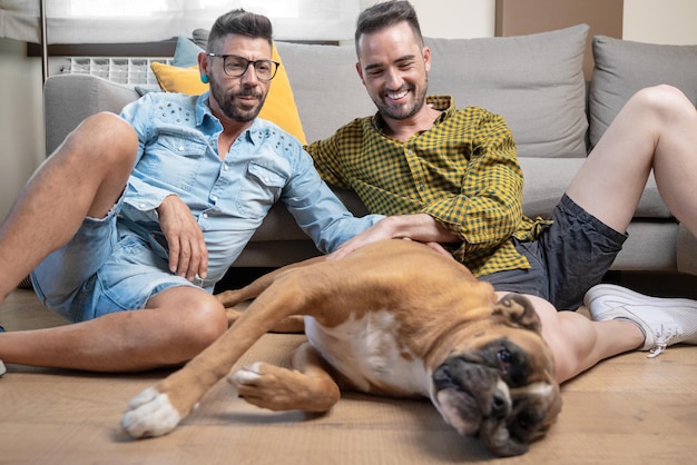 Heureux couple gay assis sur le sol et jouant avec un chien à la maison