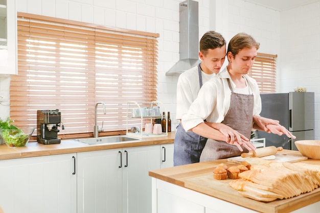 Heureux couple gay caucasien faisant du pain ensemble Une personne mélange la farine devant Et une autre personne regarde par derrière dans la cuisine à la maison Relations LGBT Concept de couple gay
