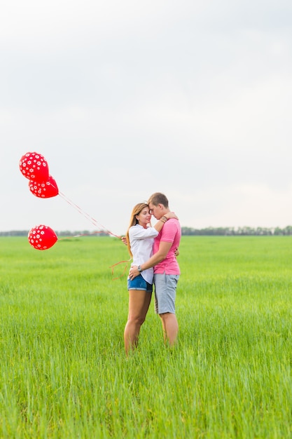 Heureux couple homme et femme amoureux habillé dans un style campagnard tenant un ballon rouge.