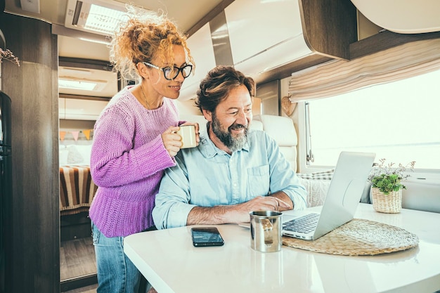 Heureux couple homme et femme travaillant et utilisant ensemble un ordinateur portable à l'intérieur d'un camping-car planifiant une destination de vacances et vivant un mode de vie vanlife en liberté Les gens voyagent et tourisme