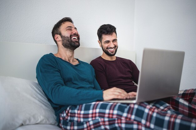 Heureux couple d'hommes homosexuels utilisant un ordinateur portable pendant l'isolement de verrouillage - Focus sur l'homme droit