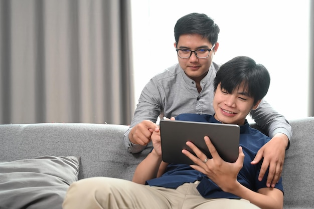 Heureux d'un couple homosexuel embrassant et utilisant une tablette numérique ensemble dans le salon Concept LGBT homosexuel