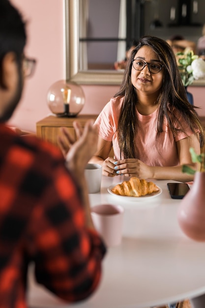 Heureux couple indien prenant son petit déjeuner et bavardant ensemble dans la cuisine amitié rencontres et famille