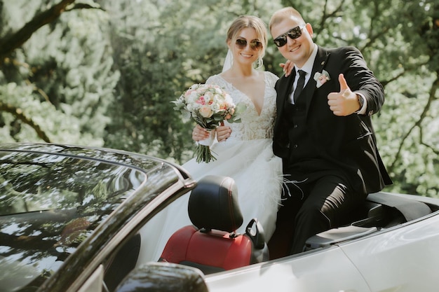 Heureux couple de jeunes mariés élégant posant dans la voiture