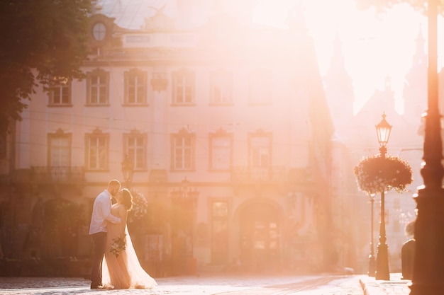 Heureux couple de jeunes mariés étreignant et embrassant dans la rue de la vieille ville au coucher du soleil magnifique mariée dans une robe de mariée avec un beau marié