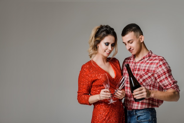 Heureux couple joyeux célébrant la tenue de verres avec champagne et pétards sur gris