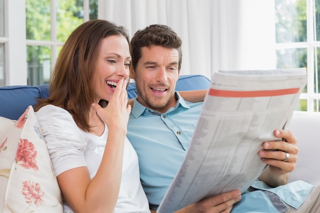 Heureux couple lisant le journal sur le canapé