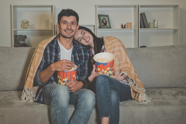 L'heureux couple mange du pop-corn et regarde un film sur le canapé