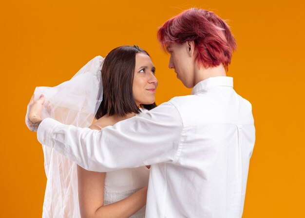 Heureux couple de mariage marié et mariée en robe de mariée sous voile, le marié regarde d'abord sa mariée