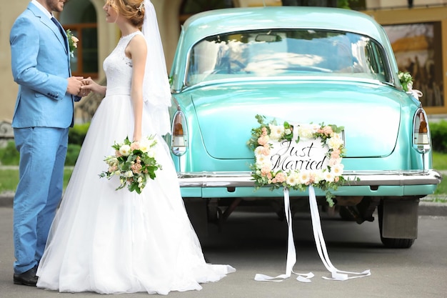 Photo heureux couple de mariage près d'une voiture décorée à l'extérieur