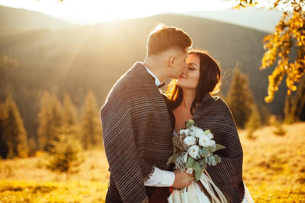 Heureux couple de mariage restant et s'embrassant sur le magnifique paysage avec des montagnes au coucher du soleil