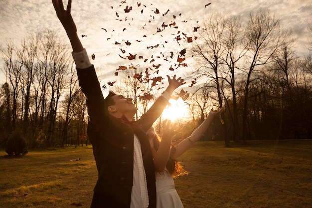 Heureux couple de mariés dans le parc acclamant et jetant des feuilles