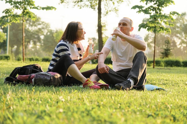 Heureux couple mature assis dans le parc sur un tapis de fitness, au repos