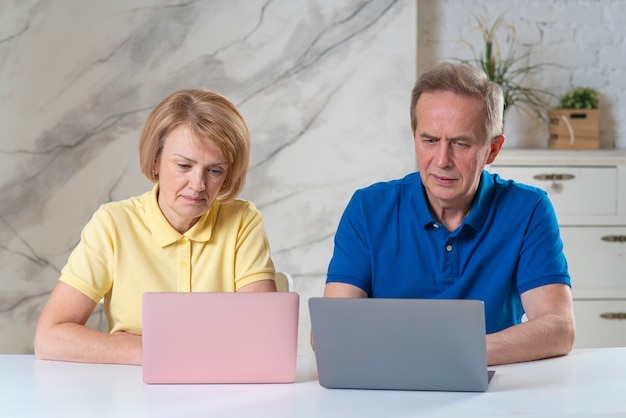 Heureux couple moderne de personnes âgées âgées travaillant ensemble sur des ordinateurs portables situés sur une table dans