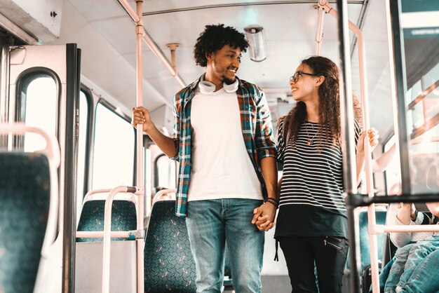 Heureux couple multiculturel debout et main dans la main tout en roulant dans le bus de la ville.