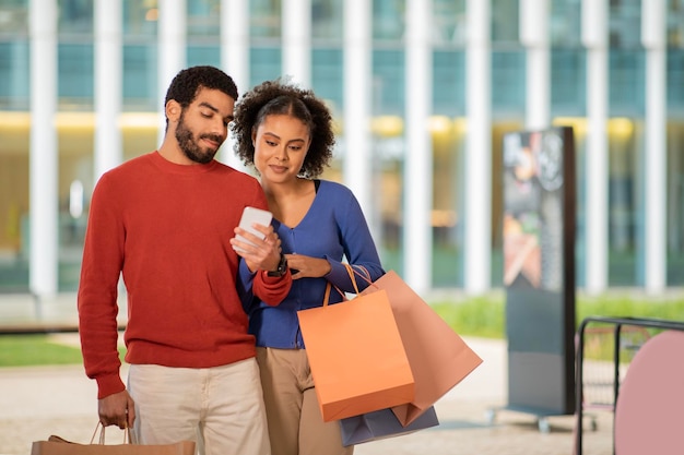 Heureux couple multiculturel faisant du shopping à l'aide d'un téléphone portable debout à l'extérieur