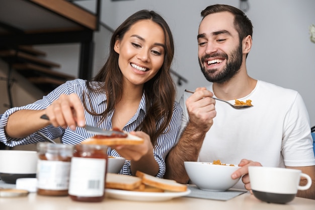 Heureux couple multiethnique prenant son petit déjeuner dans la cuisine