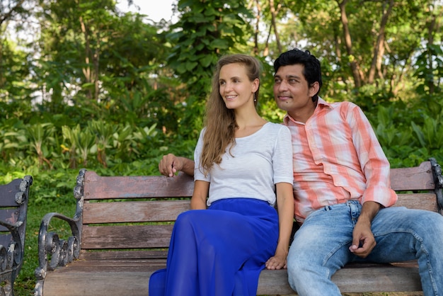 Heureux couple multiethnique souriant et pensant en position assise