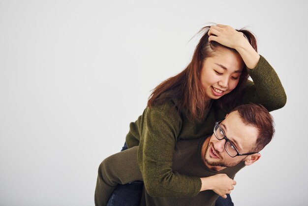 Heureux couple multiethnique en vêtements décontractés s'amuser ensemble à l'intérieur dans le studio. Mec caucasien avec petite amie asiatique.