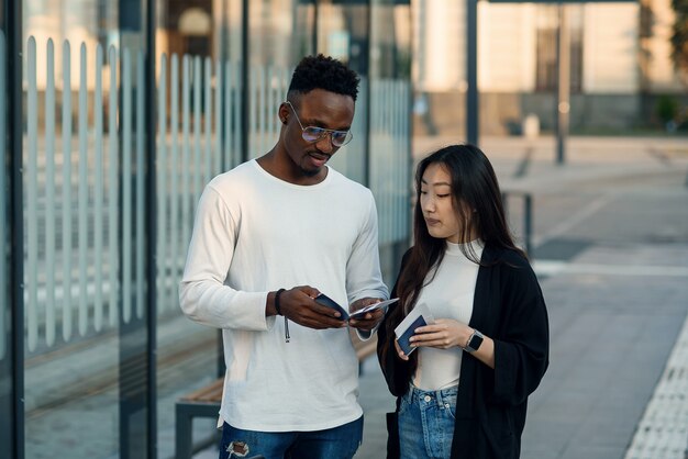 Heureux couple multiracial regarde la carte d'embarquement vérifier l'heure de départ à l'arrêt près de l'aéroport. Concept de voyage de vacances.