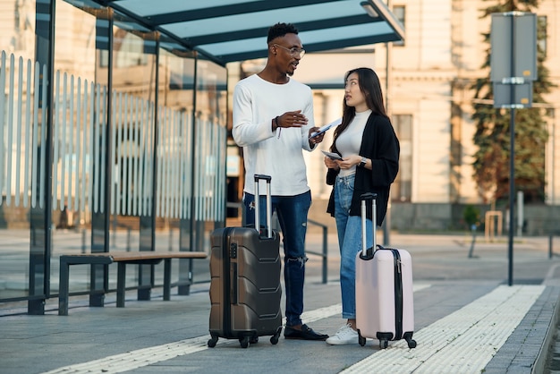 Heureux couple multiracial regarde la carte d'embarquement vérifier l'heure de départ à l'arrêt près de l'aéroport.