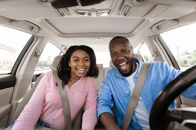 Heureux couple noir assis dans la voiture en regardant la caméra