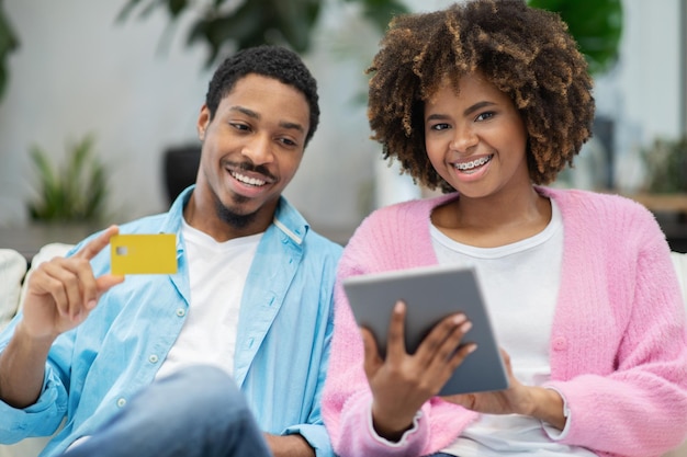 Heureux couple noir faisant ses courses à la maison à l'aide d'une carte bancaire pour tablette