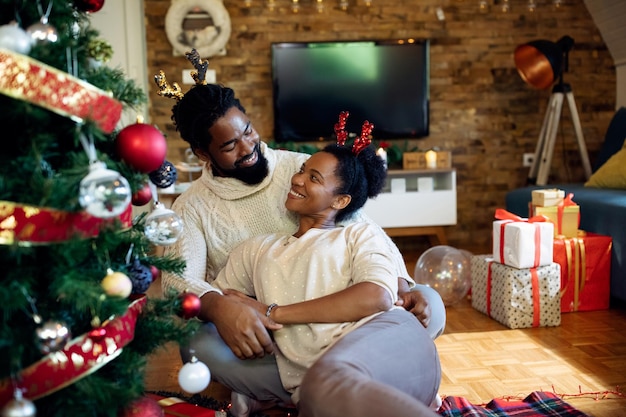 Heureux couple noir parlant tout en se relaxant près de l'arbre de Noël à la maison