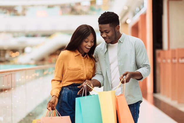 Heureux couple noir tenant des sacs à provisions regardant à l'intérieur