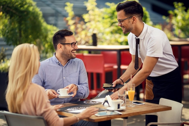 Heureux couple parlant à un serveur pendant qu'il met leur table pour dîner dans un restaurant