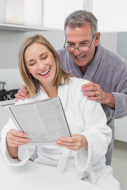 Heureux couple en peignoirs de lecture journal dans la cuisine