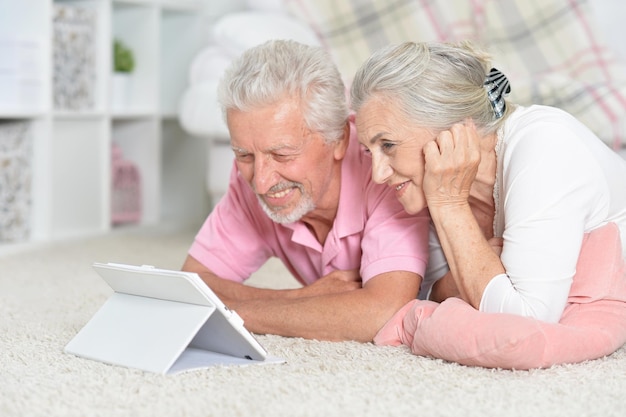 Heureux couple de personnes âgées allongé sur le sol avec une tablette moderne