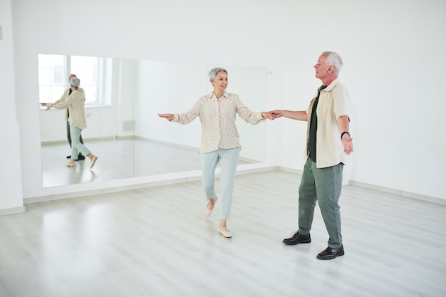 Heureux couple de personnes âgées apprenant à danser devant le grand miroir dans un studio de danse