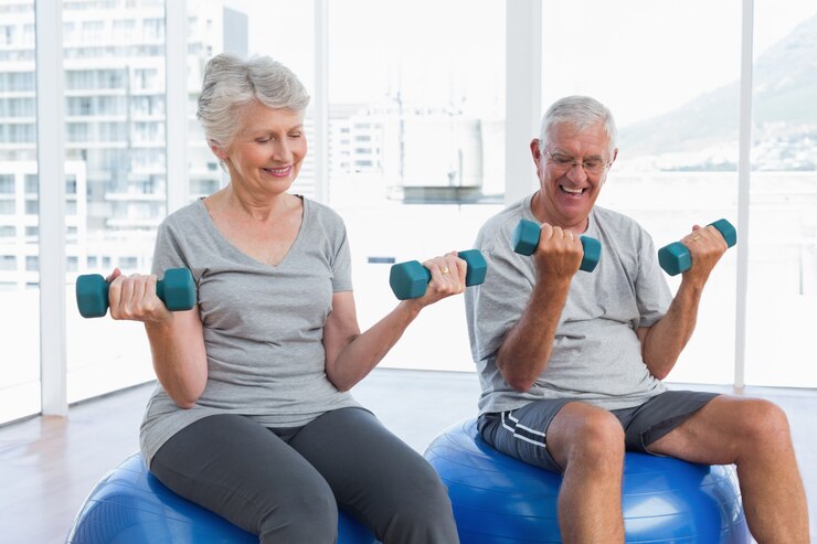 Photo heureux couple de personnes âgées assis sur des ballons de fitness avec haltères