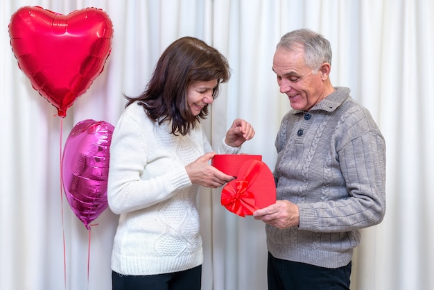 Heureux couple de personnes âgées célèbrent la Saint-Valentin. L'homme donne une boîte cadeau femme en forme de coeur