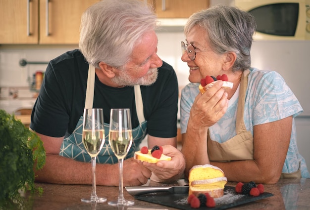 Heureux couple de personnes âgées dans la cuisine à domicile regardant dans les yeux en mangeant un gâteau aux fruits fait main avec des baies